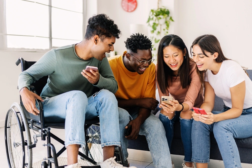 Disabled boy laughing and watching something on phone with friends